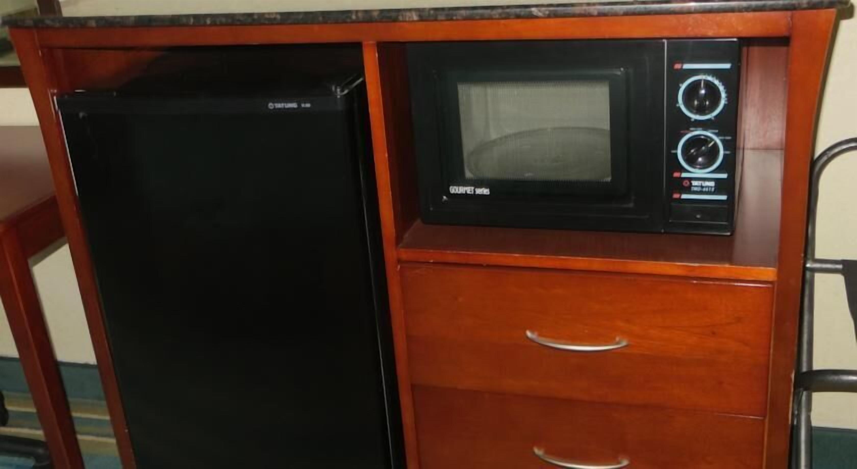 Una kitchenette compacta con un refrigerador negro y un microondas sobre una encimera de madera.