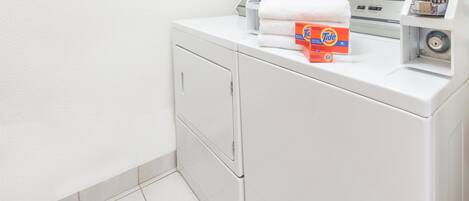 Un área de lavandería con lavadora, secadora y varios botes de detergente Tide.