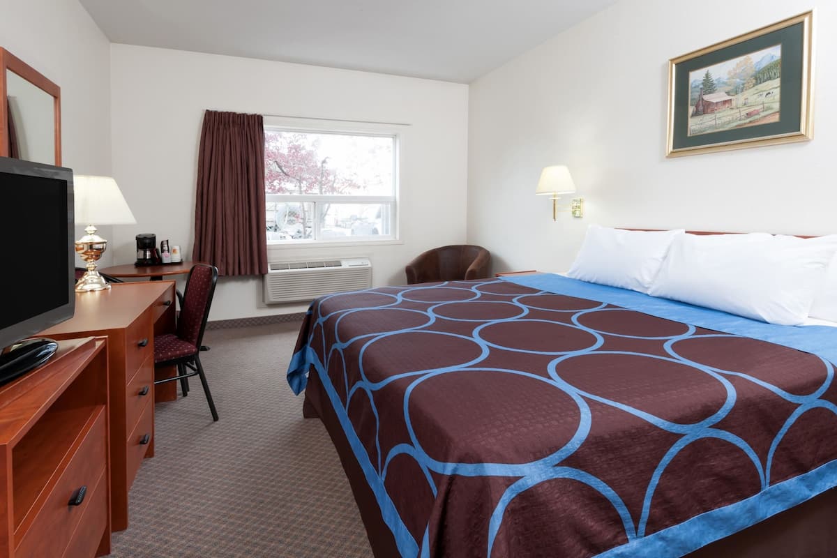 A hotel room with a bed, a desk with a TV, a chair, a window with curtains, and a painting on the wall.