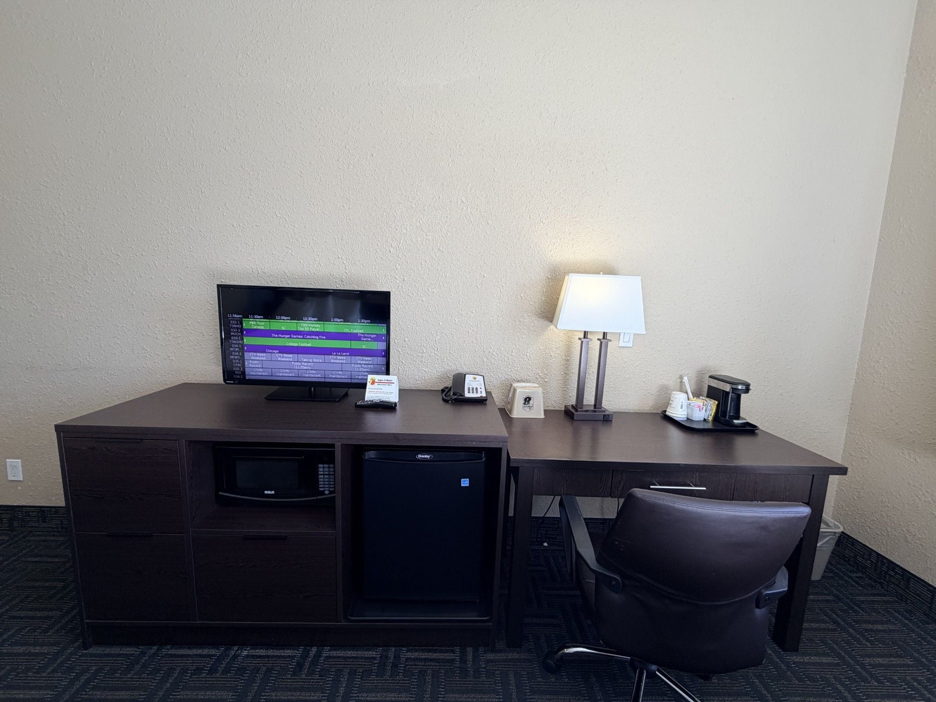 Habitación de hotel con escritorio, televisor, lámpara, teléfono, microondas y una silla.