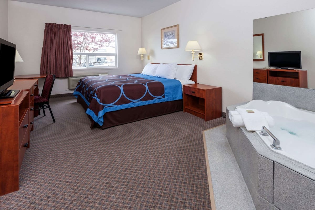 A hotel room with a bed, a desk, a chair, a TV, a bathroom with a bathtub, and a window with curtains.