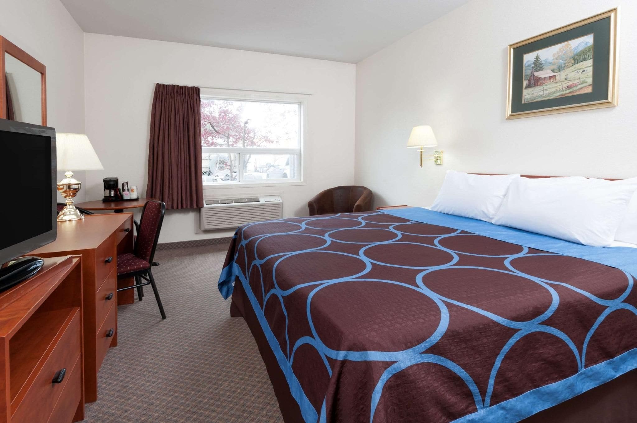 A hotel room with a bed, a desk with a television, a chair, a window with curtains, and a painting on the wall.