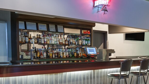 A bar area with a neon sign, a variety of liquor bottles, a cash register, and bar stools. - Super 8 by Wyndham Edmonton/West (Edmonton)
