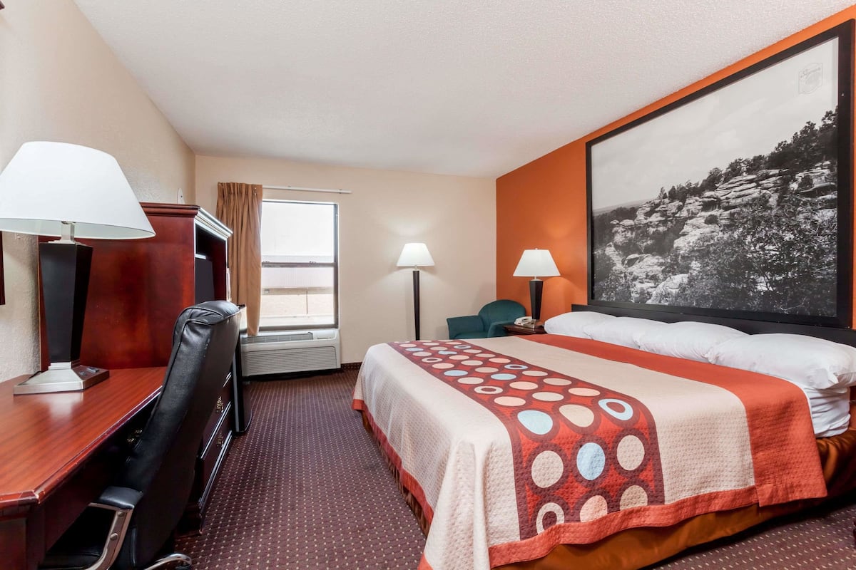 Une chambre d’hôtel avec un lit, un bureau et une chaise, une fenêtre et un grand tableau encadré au mur.