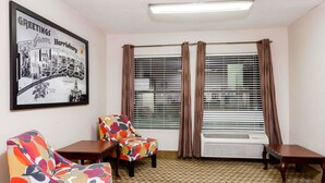 Ein Hotelzimmer mit einem gemusterten Teppich, zwei Sesseln, einem kleinen Tisch und einem gerahmten Willkommensschild.