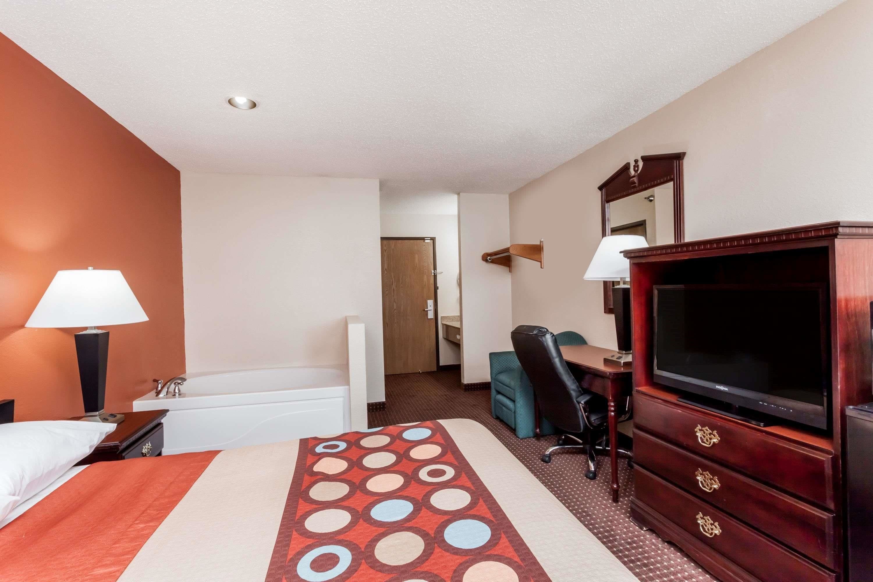 A hotel room with a bed, a desk, a chair, a television, a dresser, and a mirror.