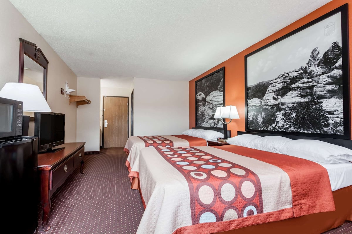 Une chambre d’hôtel avec deux lits, une télévision, un bureau et un grand tableau encadré au mur.