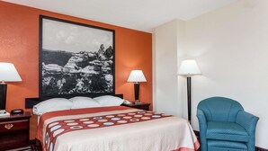 Ein Hotelzimmer mit einem großen Bett, zwei Nachttischlampen, einem Sessel und einem gerahmten Bild an der Wand.
