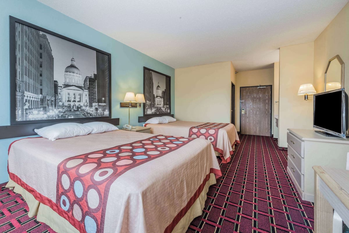 Habitación de hotel con dos camas, un televisor, un escritorio y un cuadro grande en la pared.