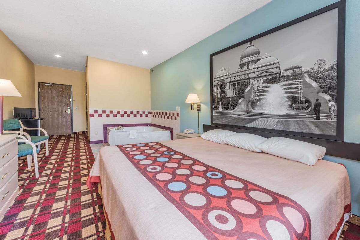 Habitación de hotel con cama, escritorio, silla, baño y un cuadro grande colgado en la pared.