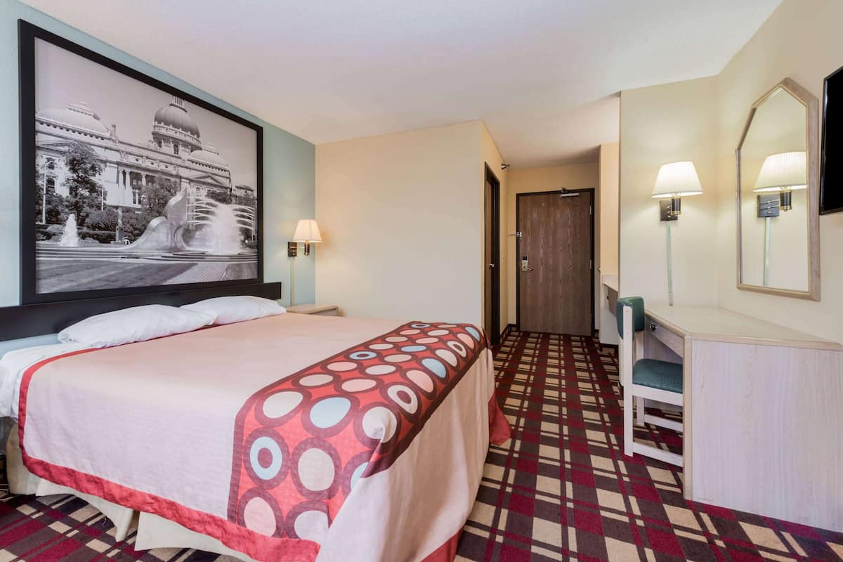 Una habitación de hotel con una cama, un escritorio, una silla, una lámpara y un cuadro grande en la pared.