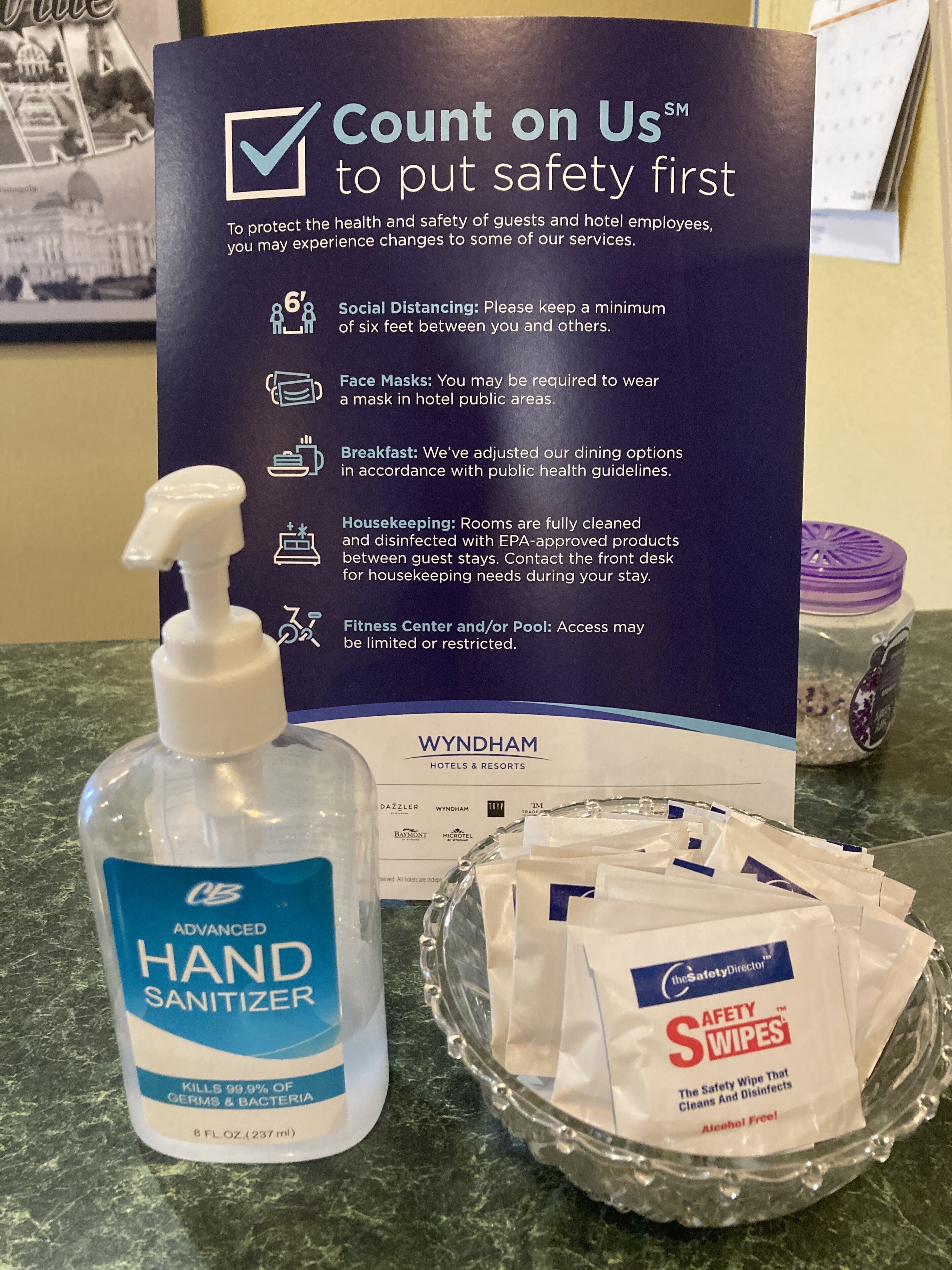 A sign with safety guidelines, a bottle of hand sanitizer, and packets of safety wipes on a counter.