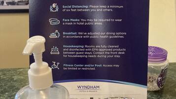 A sign with safety guidelines, a bottle of hand sanitizer, and packets of safety wipes on a counter.