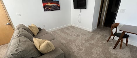 Una sala de estar con un sofá gris, un televisor de pantalla plana montado en la pared y un cuadro con un atardecer.