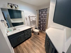 A modern bathroom with a wooden floor, a large mirror, a sink with a vanity, a toilet, and a shower curtain.