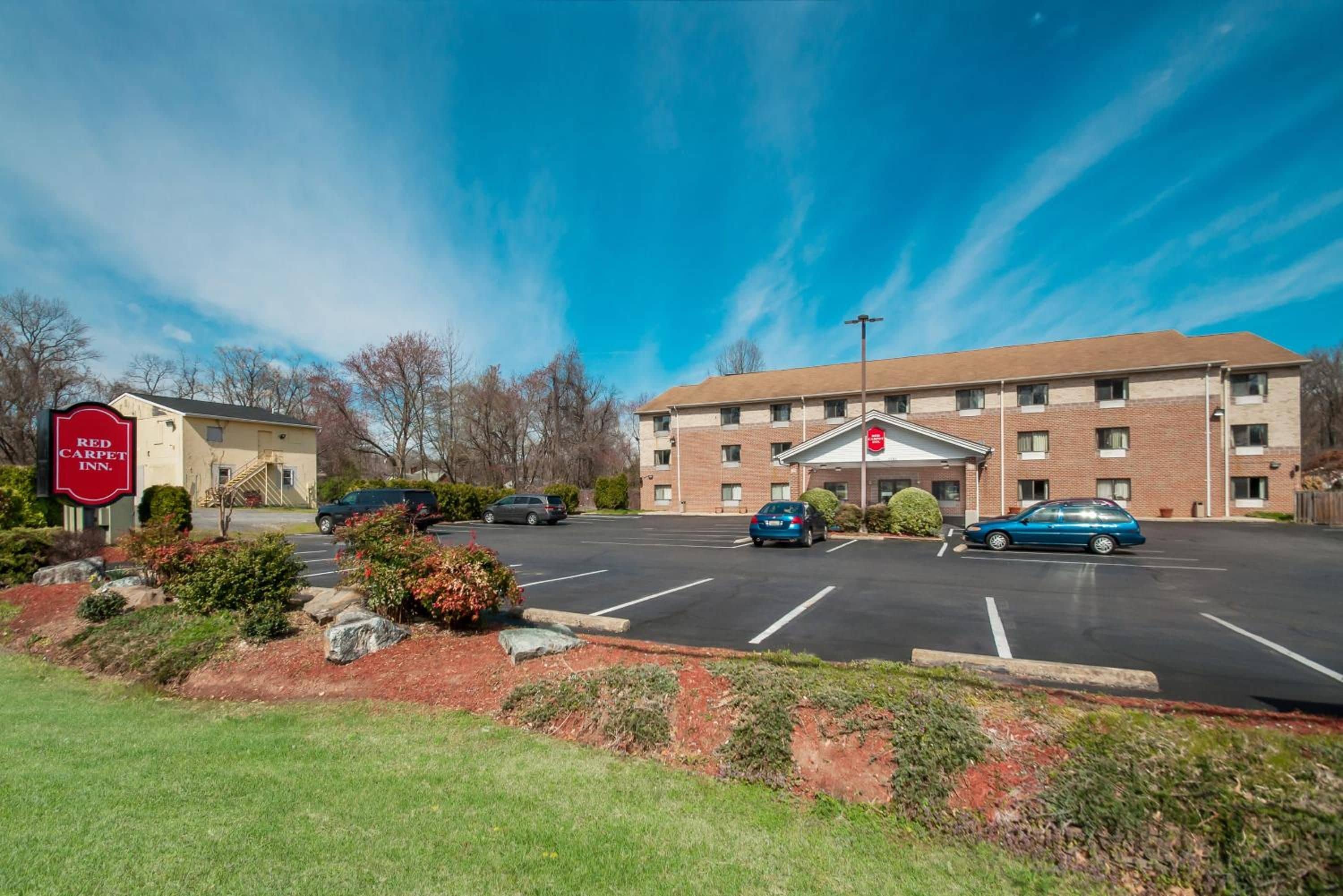 A hotel with a parking lot, a building entrance, and a sign for the Red Carpet Inn.