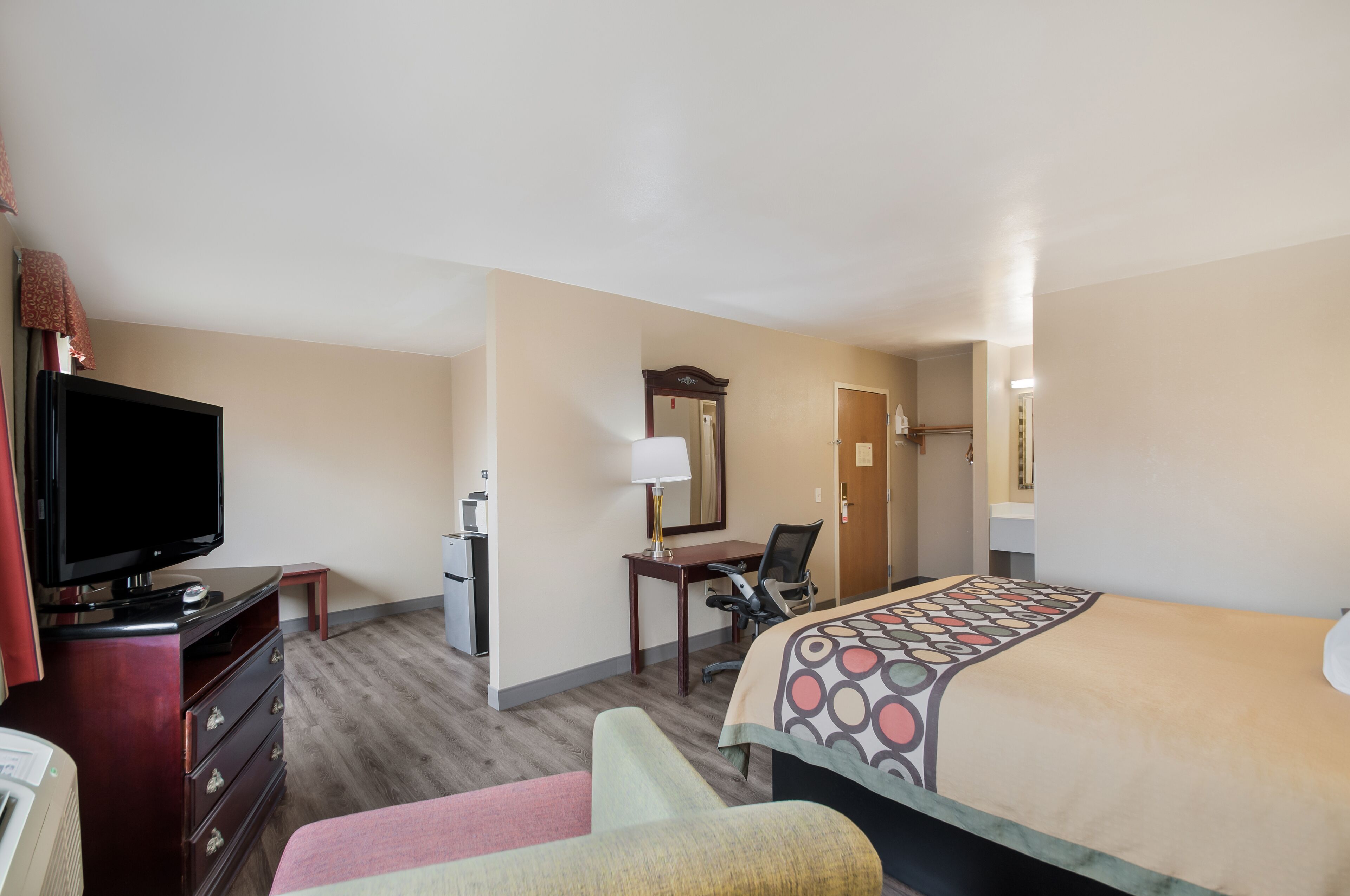 A hotel room with a bed, a desk, a chair, a television, and a dresser.