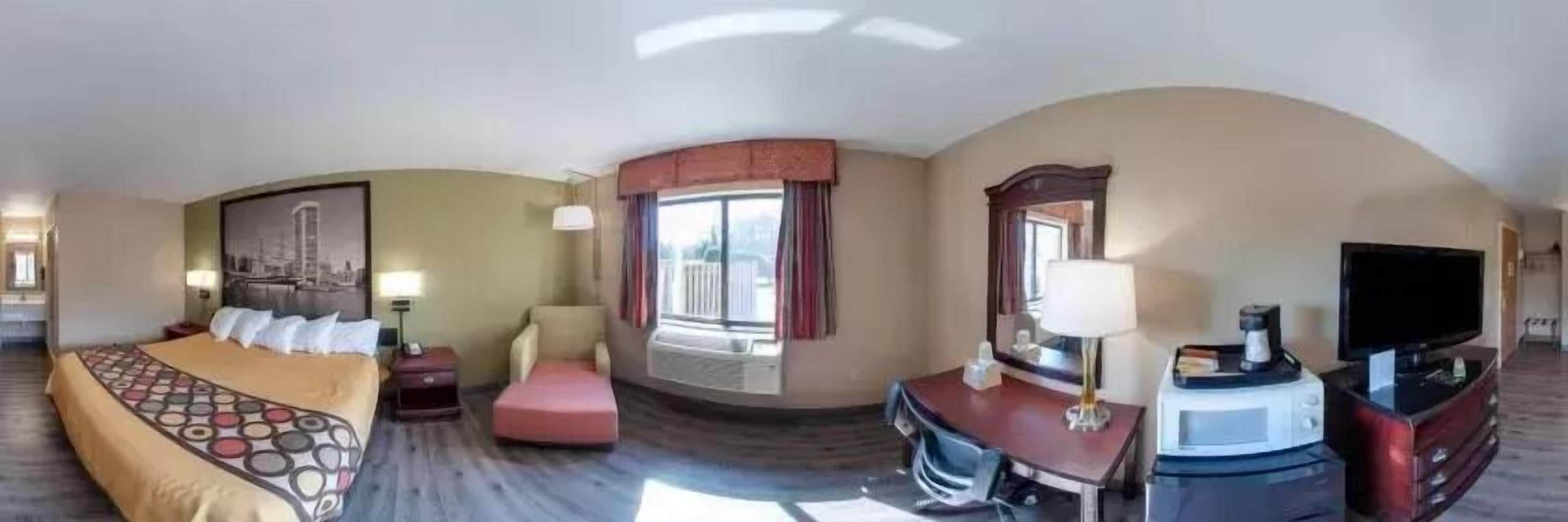 A hotel room with a bed, a desk, a chair, a TV, and a window with curtains.