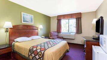 Ein Hotelzimmer mit Bett, Sessel, Schreibtisch mit Fernseher und Fenster mit Vorhängen.
