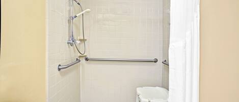 A small, white, tiled bathroom with a shower, a grab bar, and a white toilet.