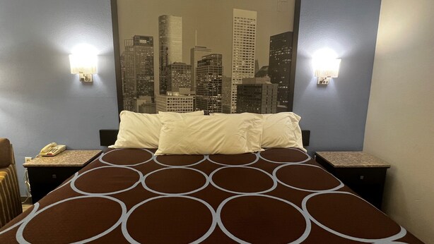 Une chambre d’hôtel avec un grand lit, deux tables de chevet, un téléphone et une vue sur la ville, que l’on peut admirer à travers un grand miroir.