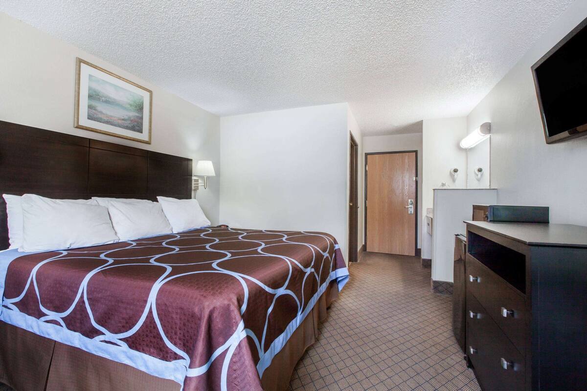Une chambre d’hôtel avec un grand lit, une commode, un téléviseur et une porte donnant sur une autre pièce.