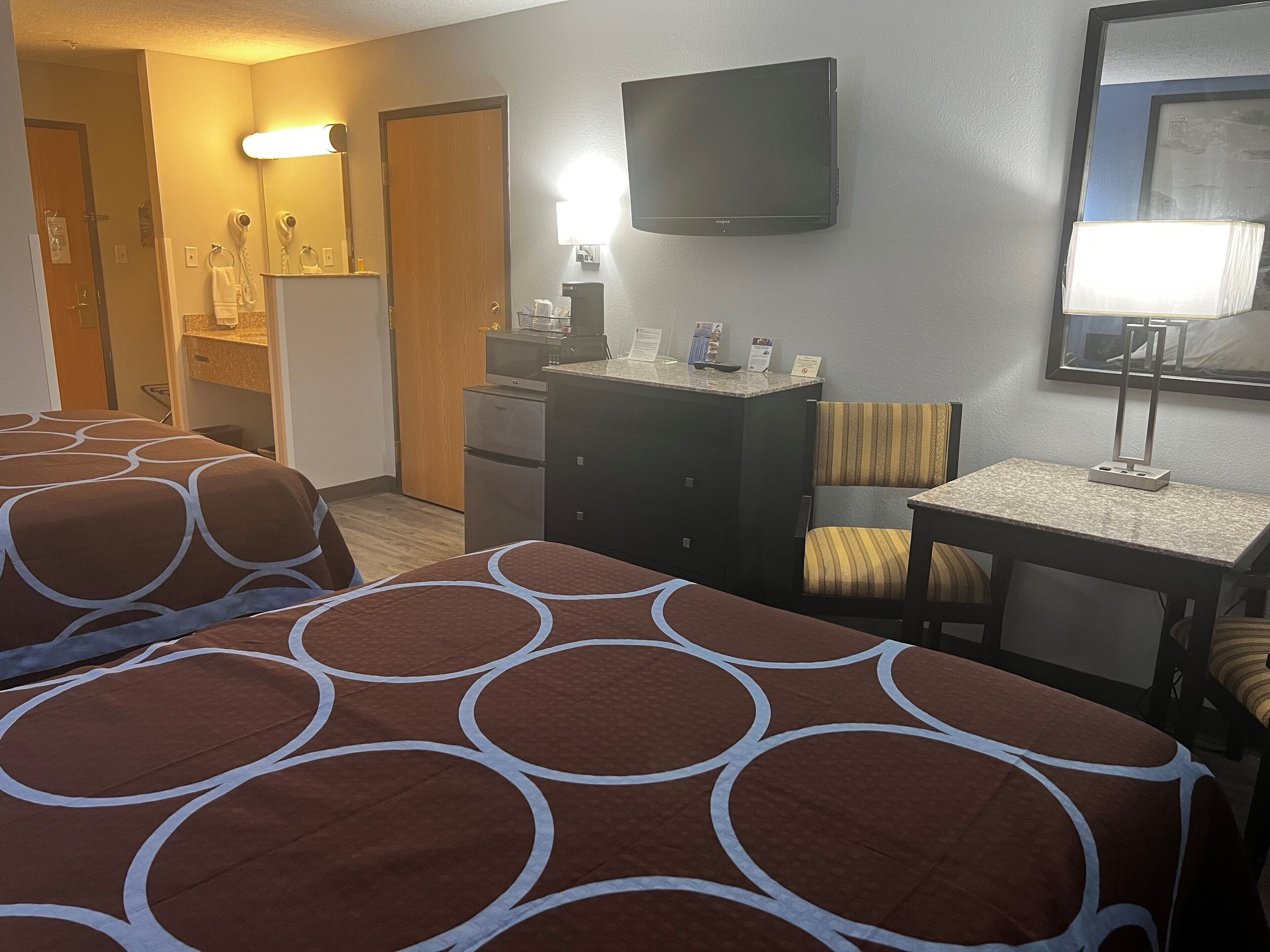 A hotel room with two beds, a desk, a chair, a television, and a mirror.