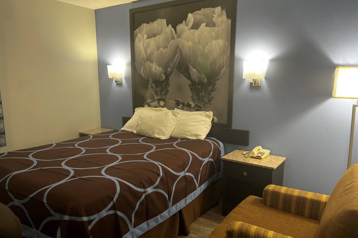 Une chambre d’hôtel comprenant un lit, une table de chevet avec un téléphone, une chaise et un luminaire fixé au mur.