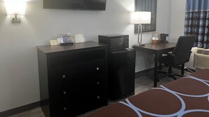 Une chambre d’hôtel équipée d’une télévision à écran plat, d’un bureau avec une lampe, d’un four à micro-ondes, d’un mini-réfrigérateur, d’une chaise et d’un lit recouvert d’une couvre-lit à motifs.