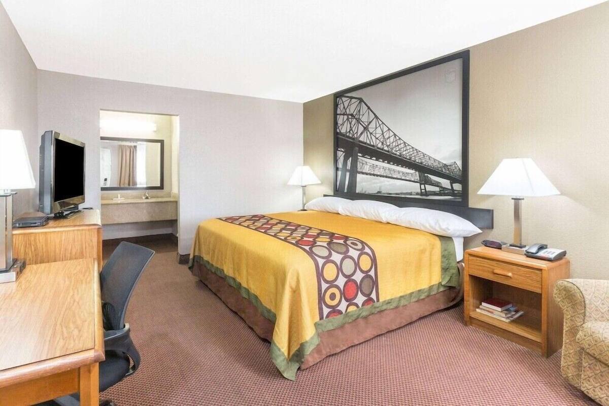 Een hotelkamer met een bed, een bureau, een stoel, een televisie, een lamp en een boekenkast.