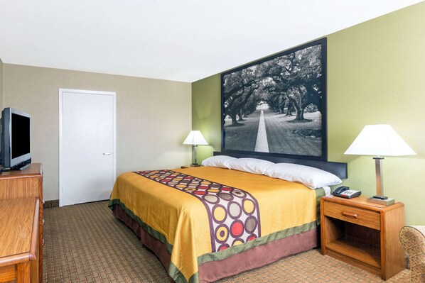 A hotel room with a bed, two bedside lamps, a TV, and a large framed picture on the wall.
