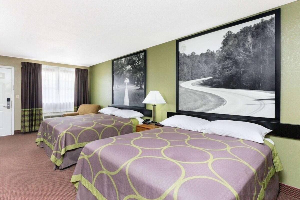 Een hotelkamer met twee bedden, een bureau, een stoel en grote, ingelijste foto’s aan de muur.