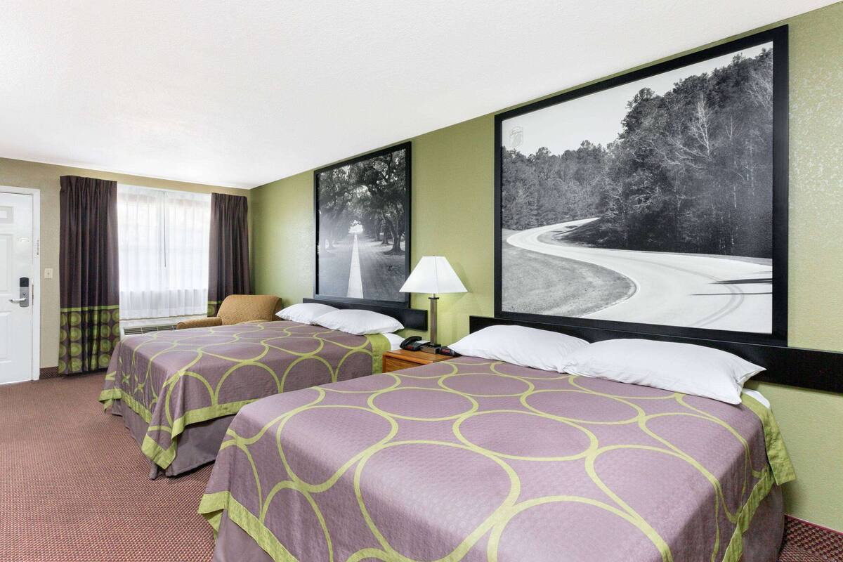 Een hotelkamer met twee bedden, een bureau, een stoel en grote afbeeldingen in lijsten aan de muur.
