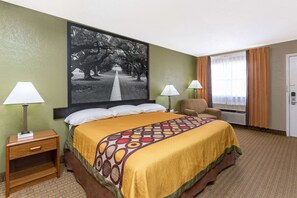 A hotel room with a large bed, two bedside lamps, a chair, a door, and a large framed picture on the wall. - Super 8 by Wyndham Tallulah LA (Tallulah)