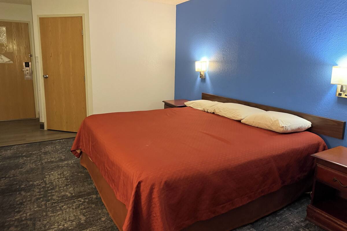 Habitació d'hotel amb un llit gran, panell de capçal de fusta, dues taules de nit i una petita taula auxiliar.