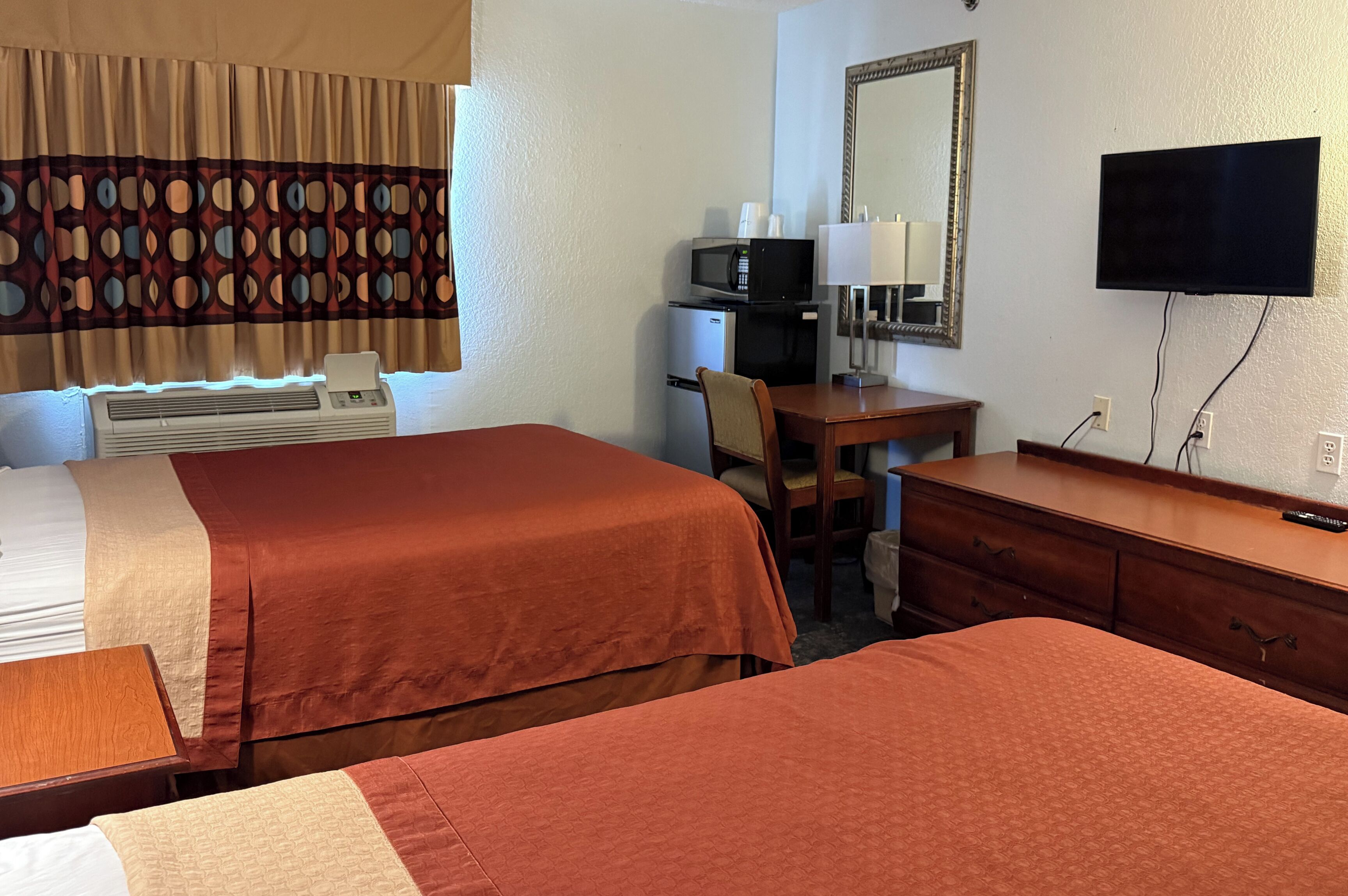 A hotel room with two beds, a desk, a chair, a television, a mirror, and a microwave.