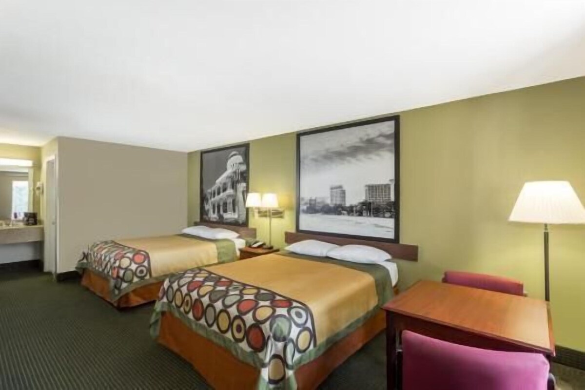 A hotel room with two beds, a desk, a chair, a lamp, and two wall-mounted lamps.