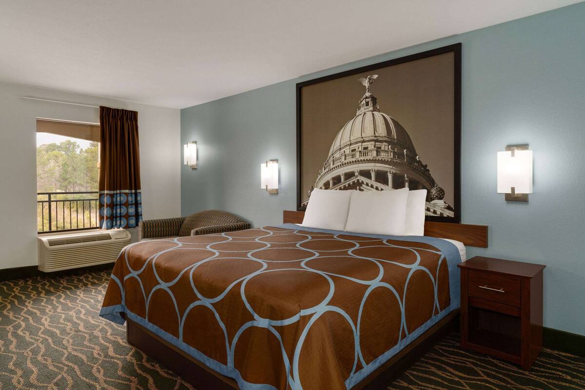 Hotelkamer met een groot bed, uitzicht op een gebouw door een raam, een klein tafeltje en een wandlamp.