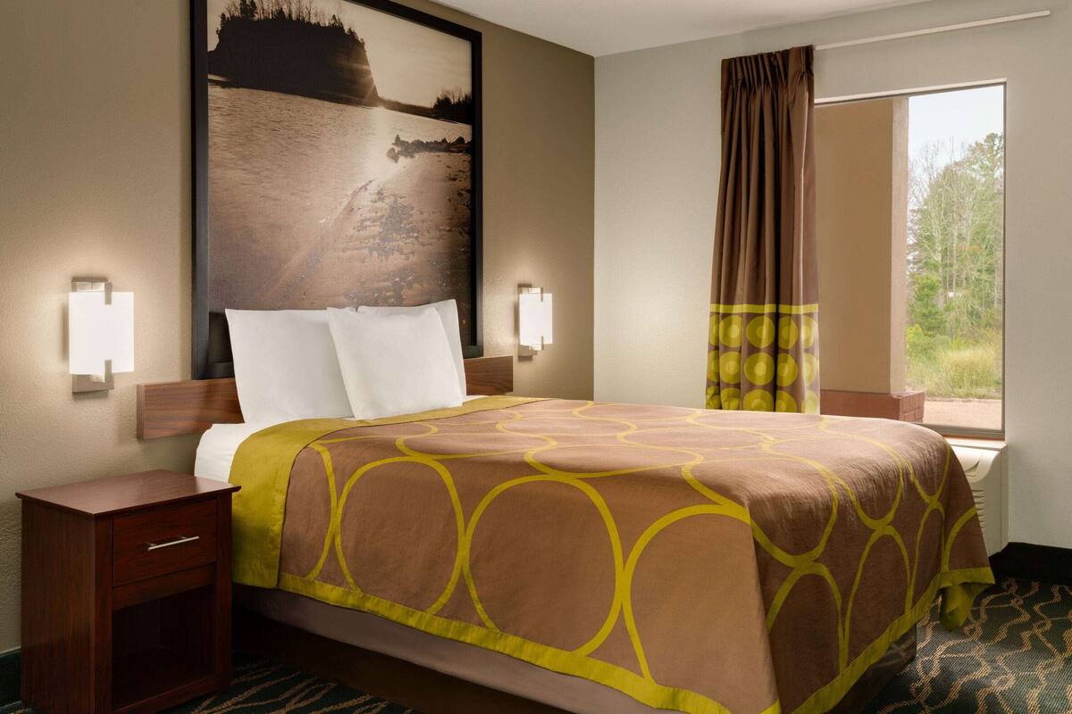 Een hotelkamer met een groot bed, nachtkastje, een wandlamp en een raam met gordijnen.
