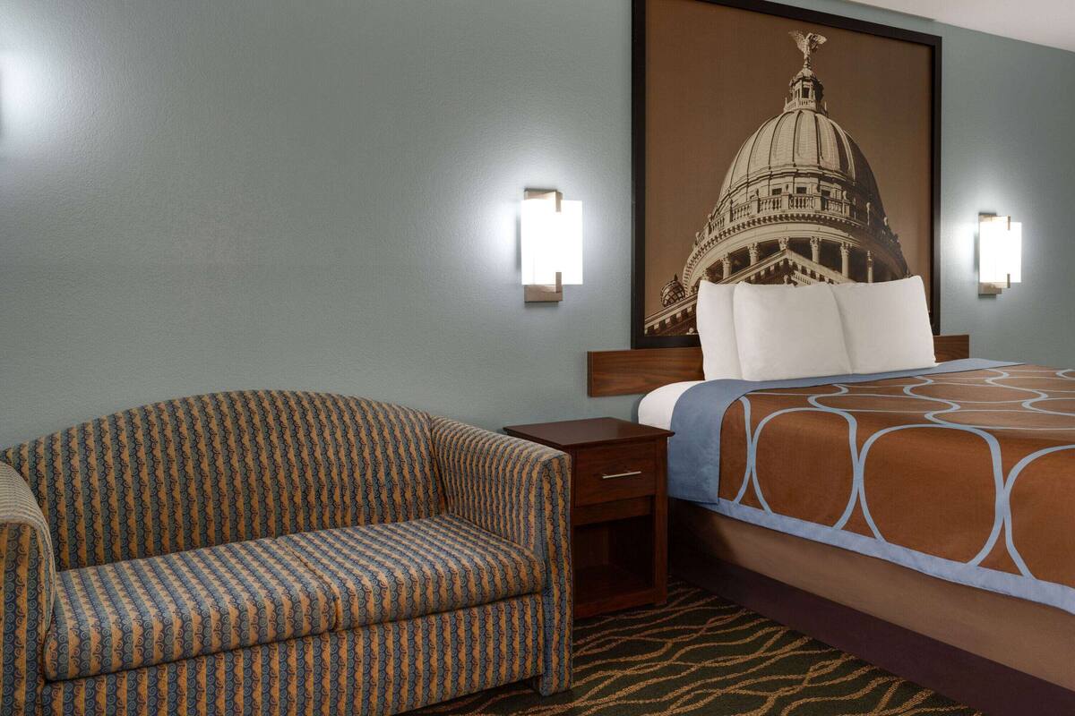 Een hotelkamer met een gestreept fauteuil, een bed met een beddengoed met dessin, een nachtkastje en een wandlamp.