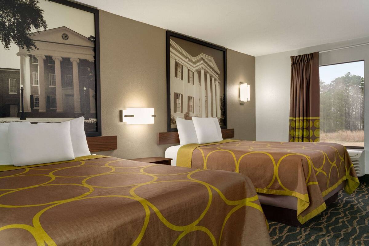 Een hotelkamer met twee bedden, een grote spiegel en uitzicht op een gebouw door het raam.
