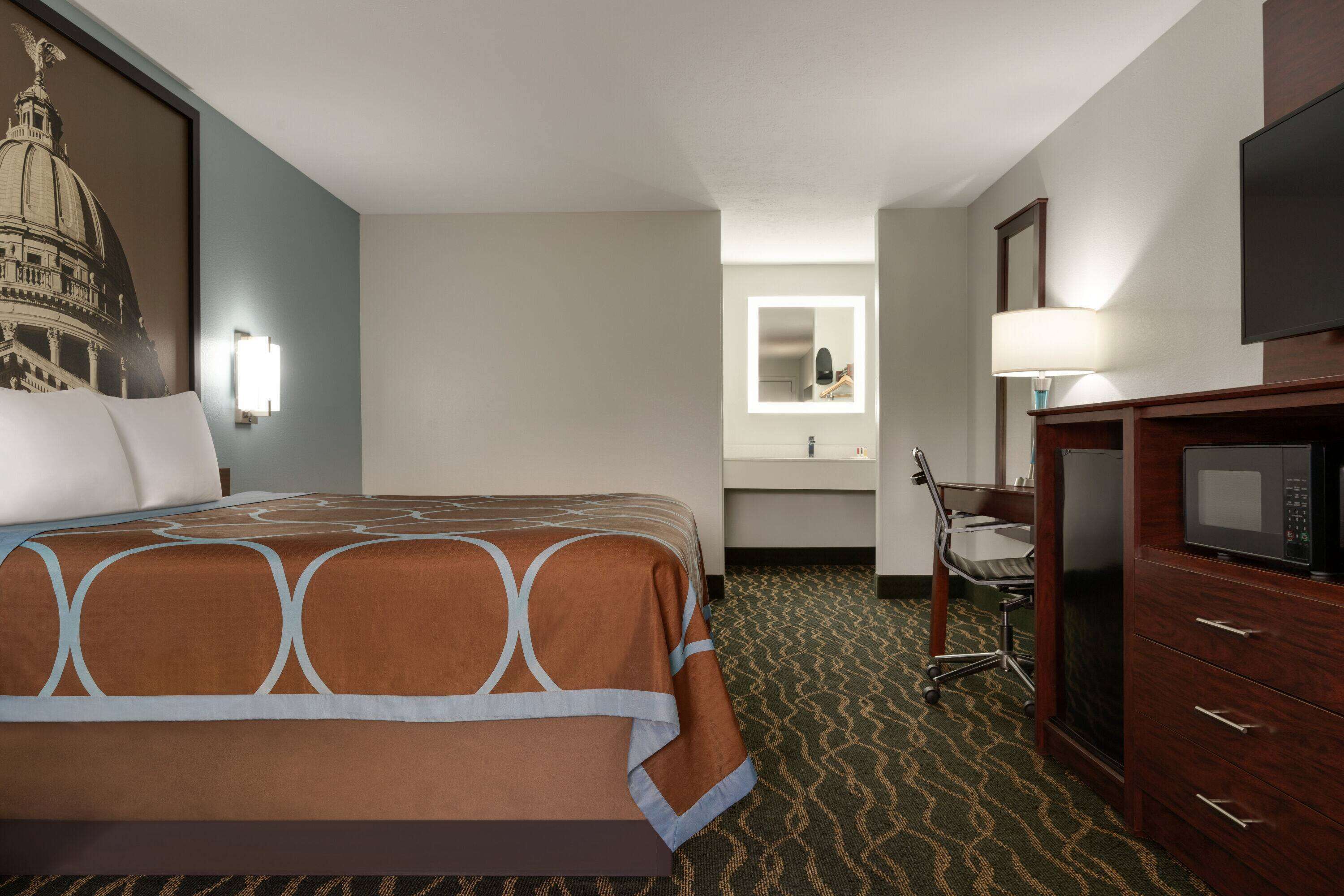 A hotel room with a large bed, a desk with a chair, a microwave, and a mirror above the sink.