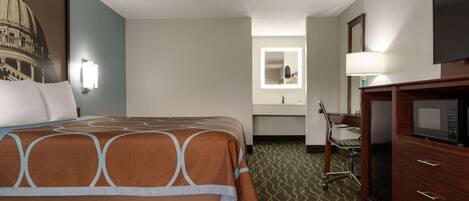 A hotel room with a large bed, a desk with a chair, a microwave, and a mirror above the sink.