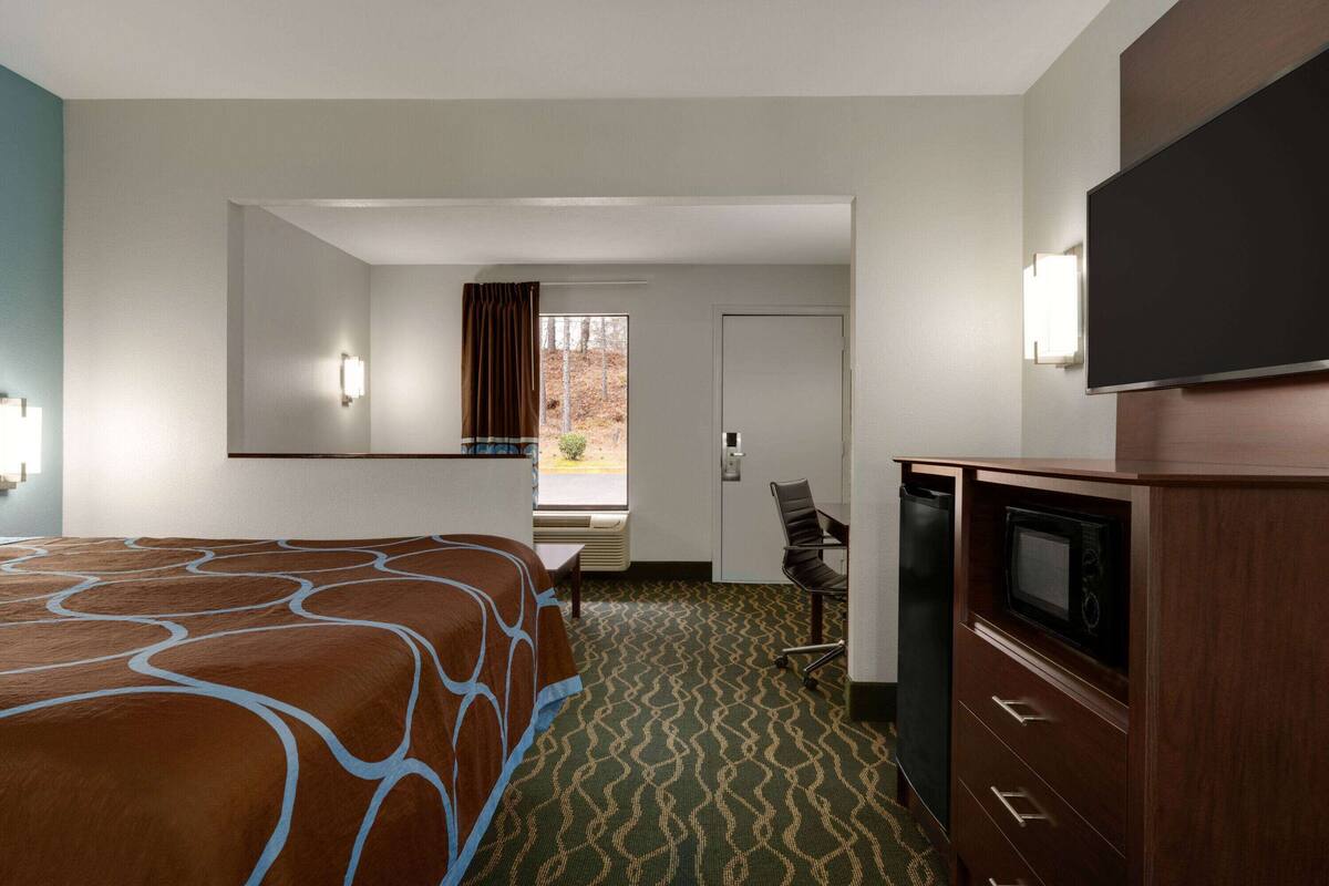 Een hotelkamer met een bed, een bureau, een stoel, een televisie en een magnetron.