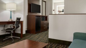 A hotel room with a desk, chair, television, minibar, and a sofa. - Super 8 by Wyndham Pearl/Jackson Airport (Pearl)
