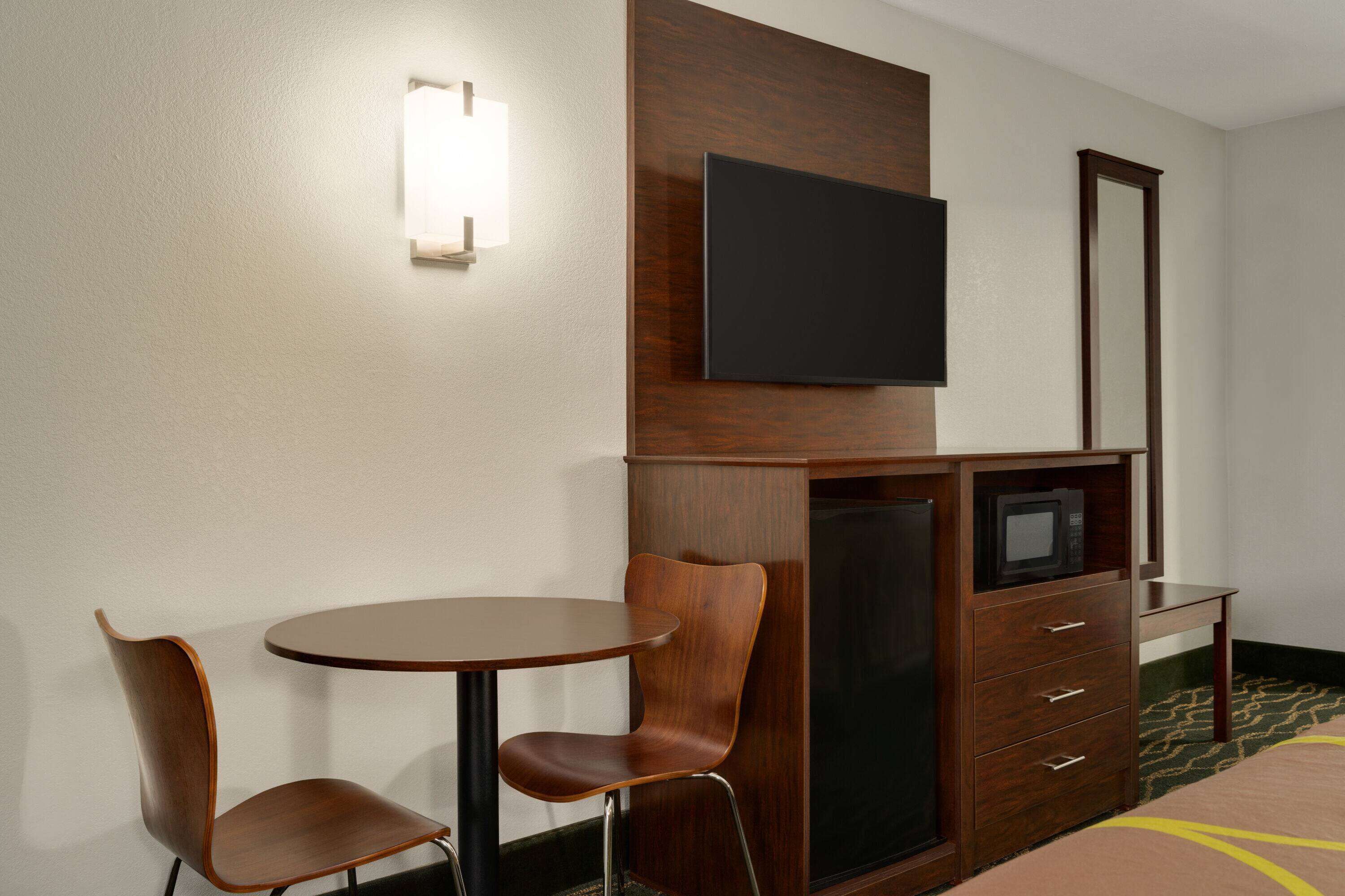 Et hotelværelse med skrivebord i træ, to stole, et fladskærms-tv, et spejl og en minibar.