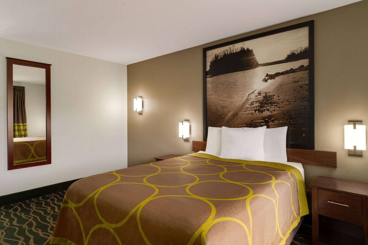 Een hotelkamer met een groot bed, een nachtkastje, een spiegel en een aan de muur hangend schilderij.