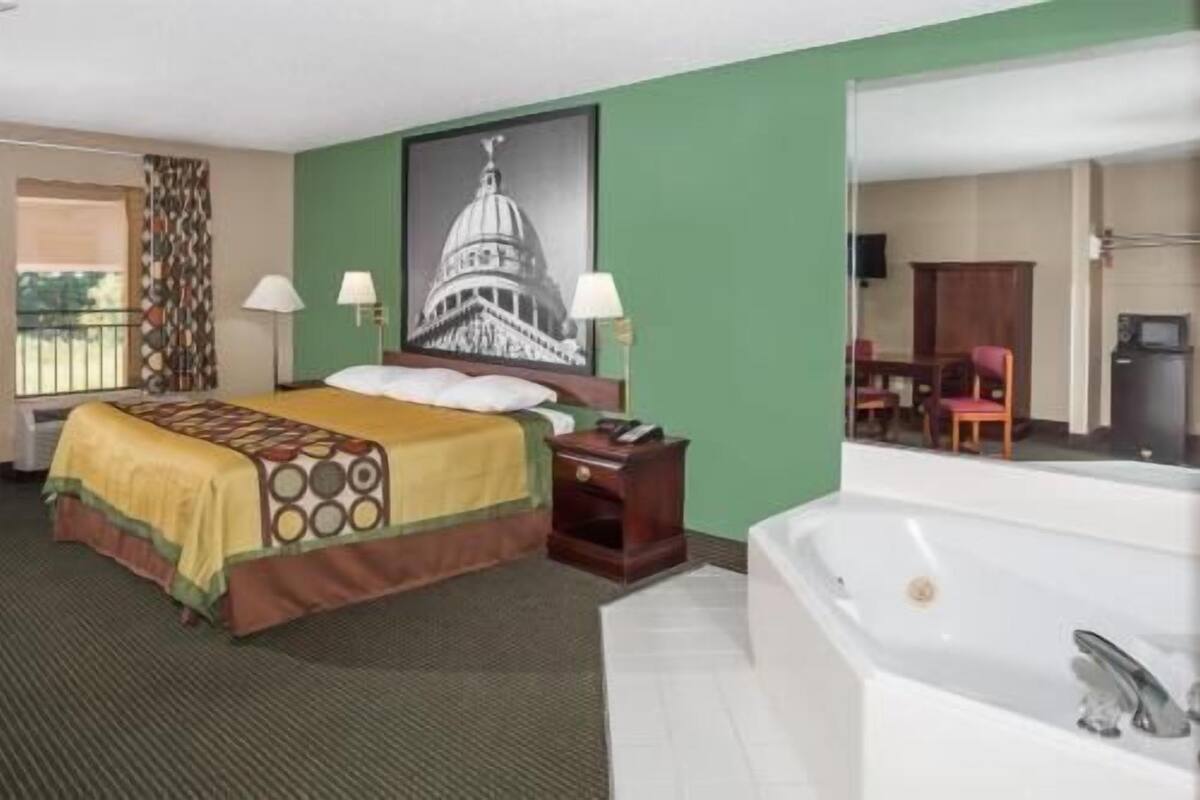 Hotelkamer met een bed, bureau, stoel, groot raam en een badkamer met bad.