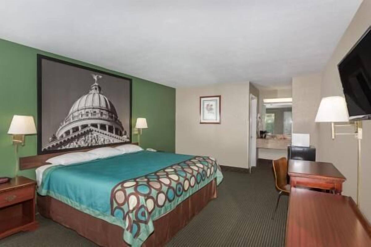 Een hotelkamer met een bed, een bureau, een stoel, een televisie, een lamp en een ingelijst schilderij aan de muur.