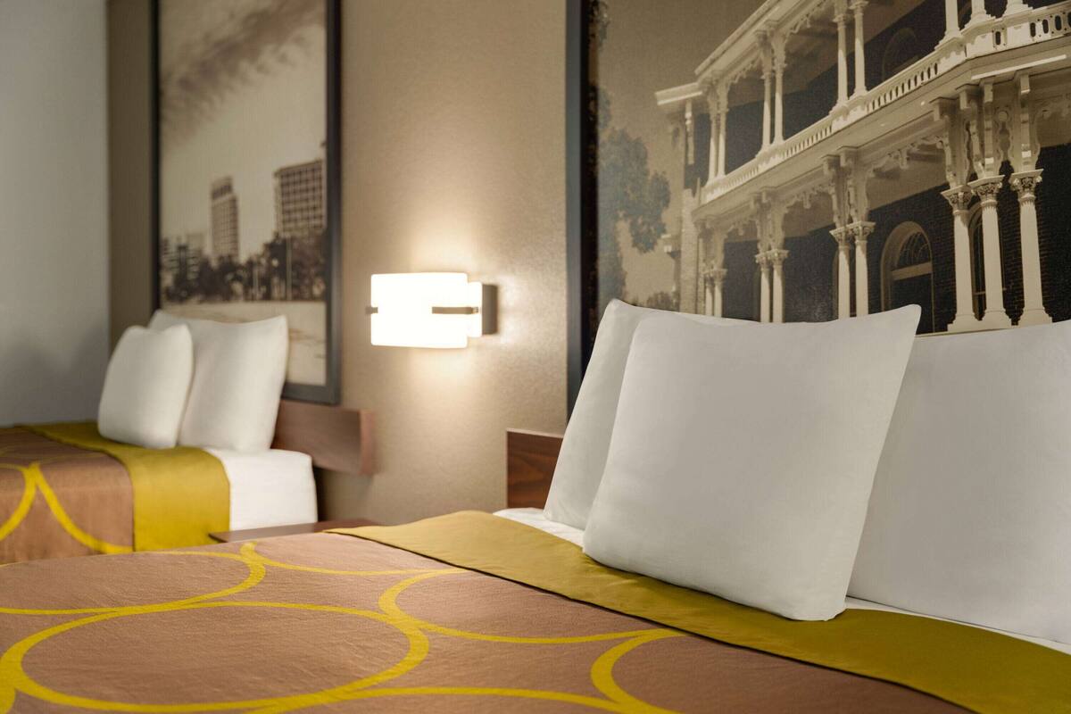 Een hotelkamer met een bed, kussens, een hoofdeinde en een wandlamp.